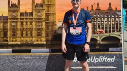 A picture of myself (Luc Shelton) posing with my medal after running the ASICS London 10K. I'm standing in front of a photo backdrop.